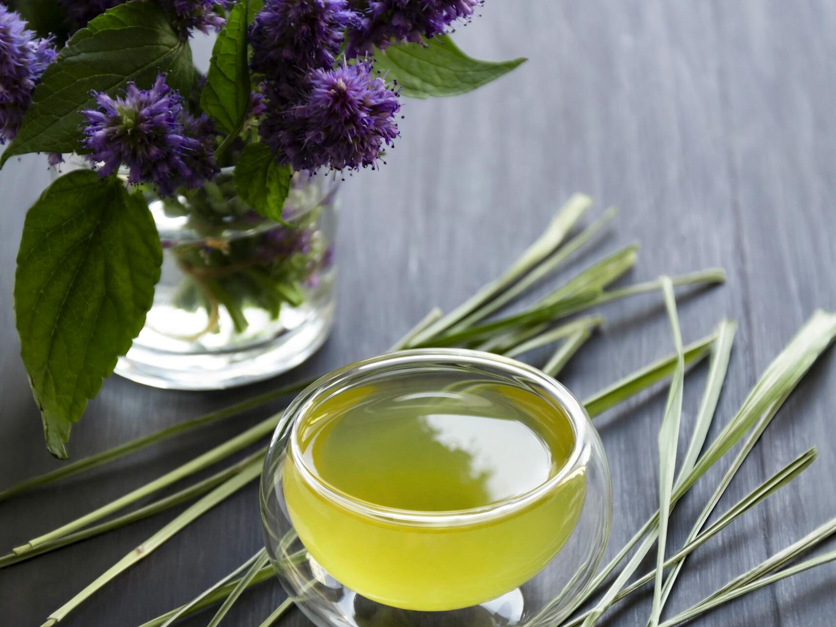 A refreshing herbal tea surrounded by purple Korean mint flowers and lemongrass on a slate background.